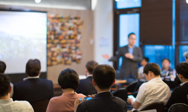 Presenter,With,Hands,Pointing.,Blurred,De-focused.,Unidentifiable,Business,Audience,People