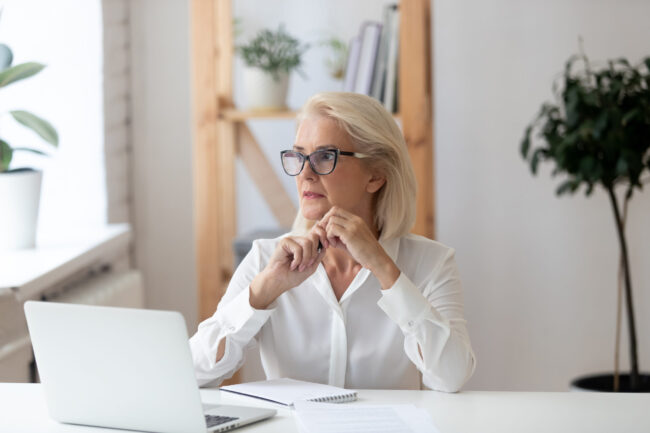 Thoughtful,60,Years,Old,Businesswoman,Using,Laptop,,Pondering,Online,Project